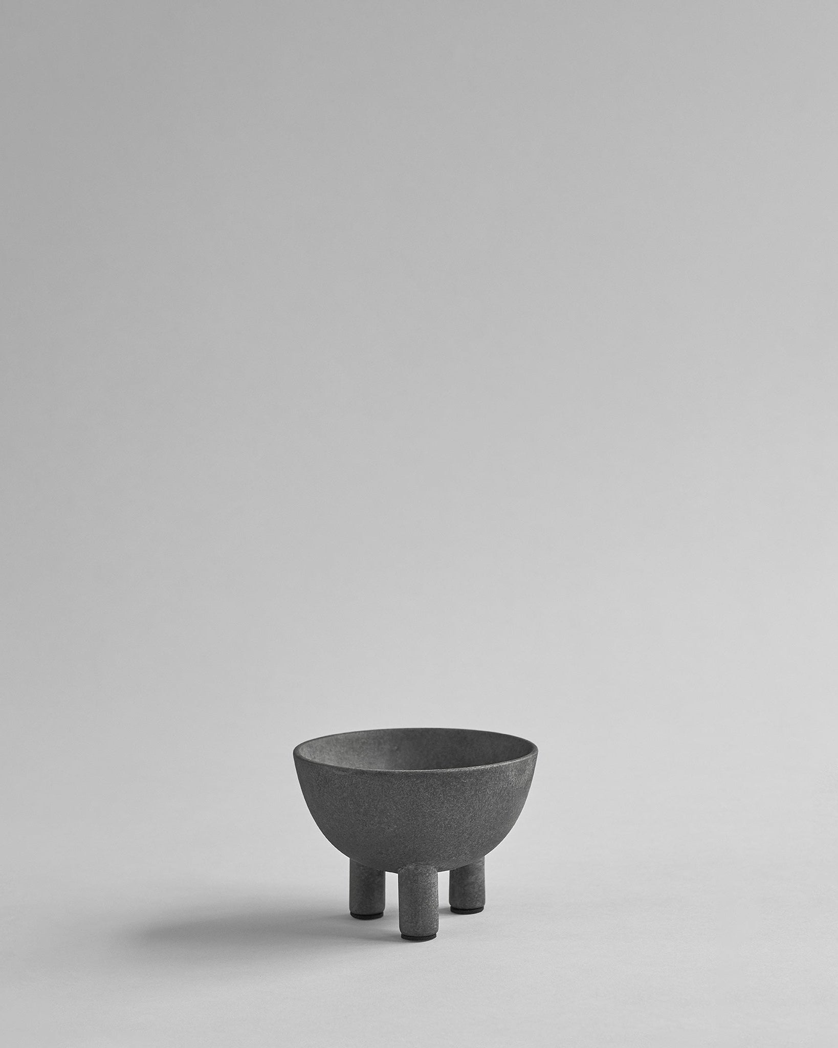 Dark gray ceramic bowl with three legs on a light gray background