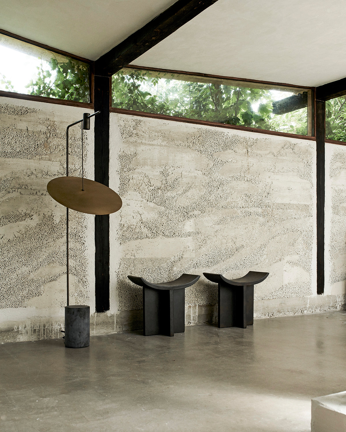 Two curved fibre concrete stool in front of a concrete wall and a beautoful reflection lamp by 101 copenhagen curated by Numa Home.