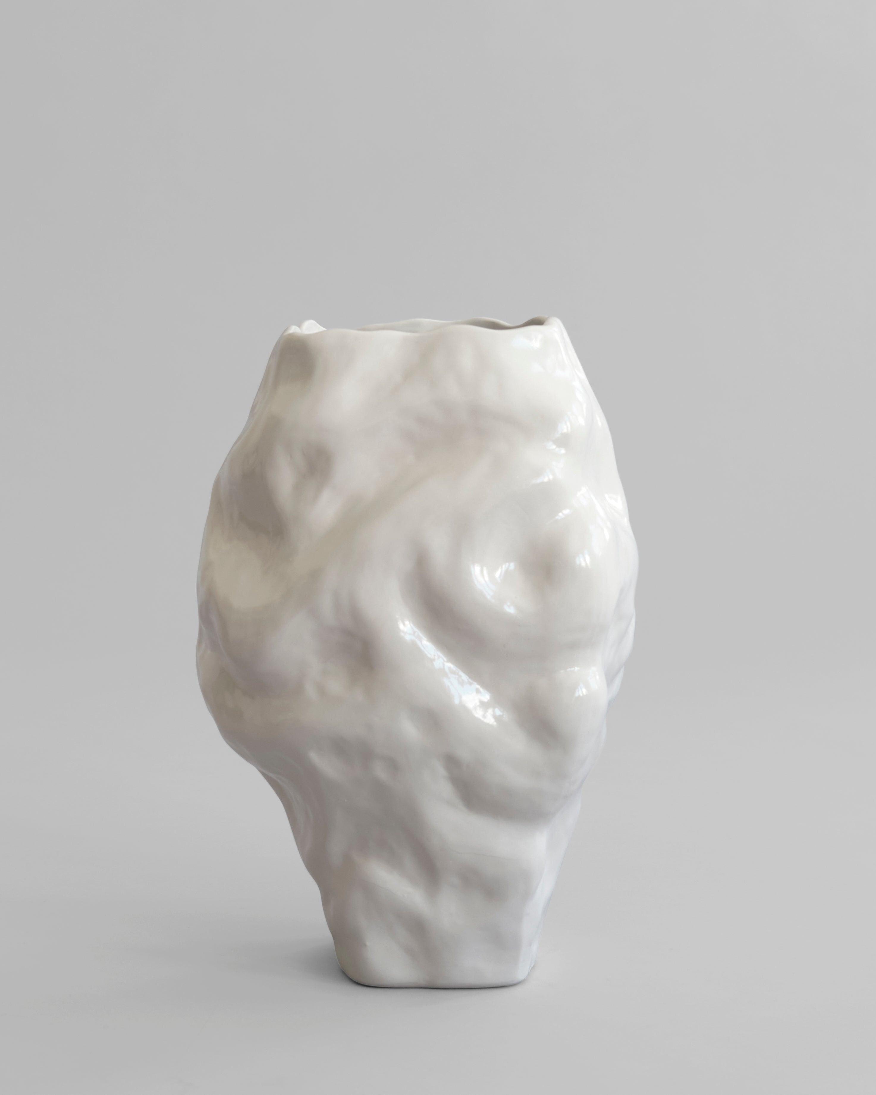 White ceramic vase with textured surface on a gray background. Katachi Vase, Big by 101 Copenhagen. Sculptural vase inspired by Japanese “shape”, available in High Glaze Birch ceramic and Clear or Smoked Forest mouth-blown glass. Fully waterproof, curated by Numa Home.