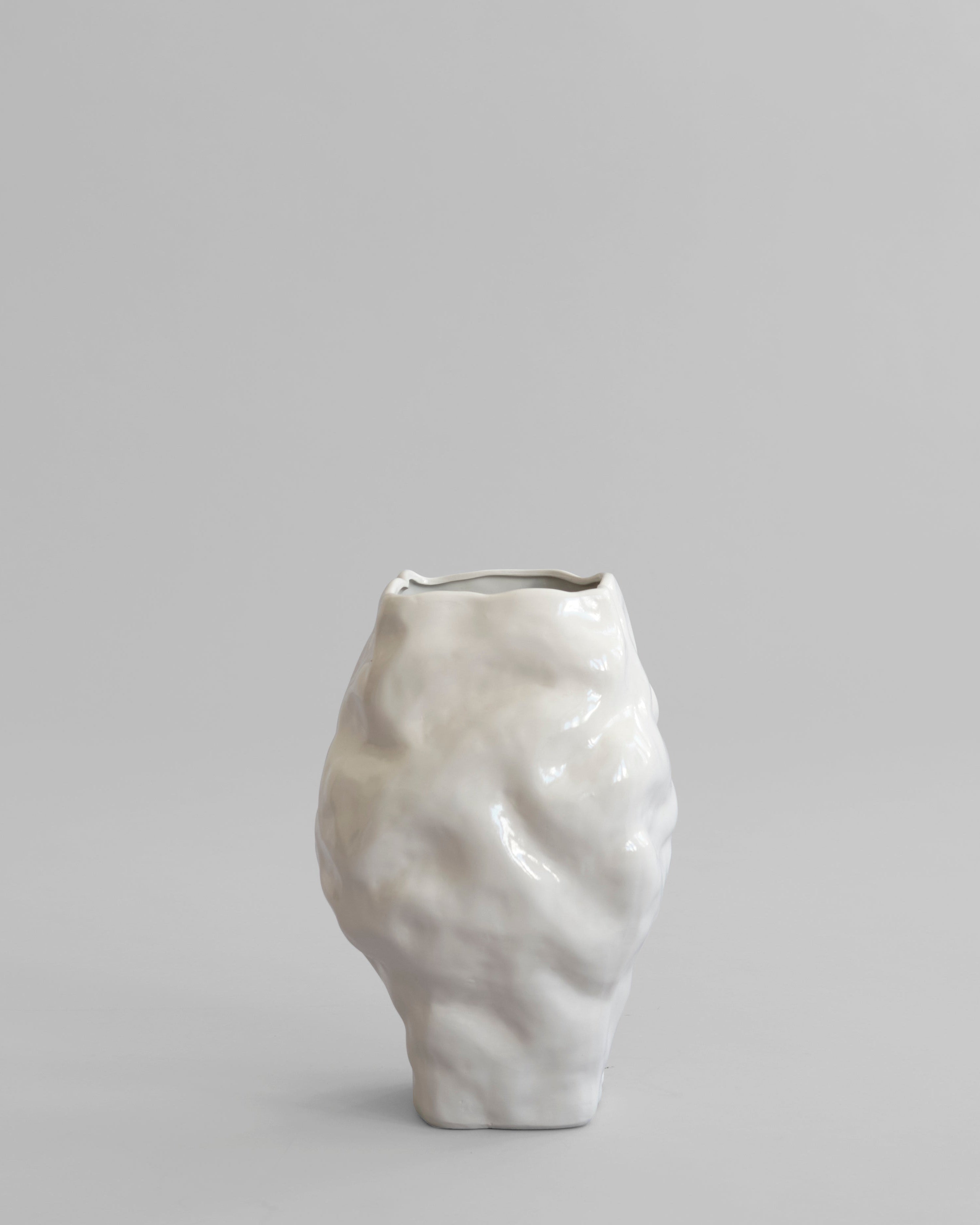 White ceramic vase on a gray background. Katachi Vase, Medio by 101 Copenhagen. Sculptural vase inspired by Japanese “shape”, available in High Glaze Birch ceramic and Clear or Smoked Forest mouth-blown glass. Fully waterproof – curated by Numa Home.