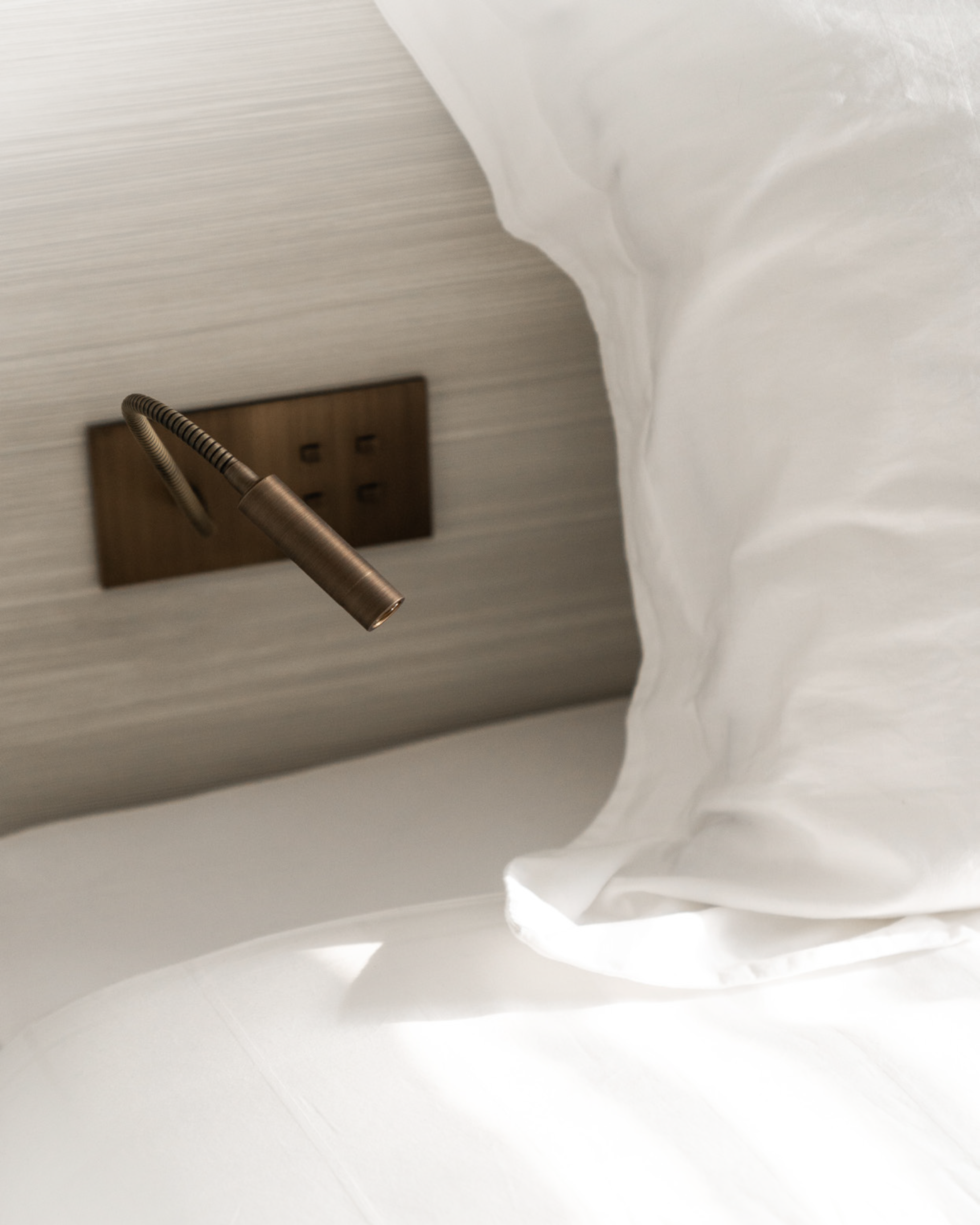 Close-up of a bed with white bedding and a brass reading light in brushed brass patina with 4 push buttons.