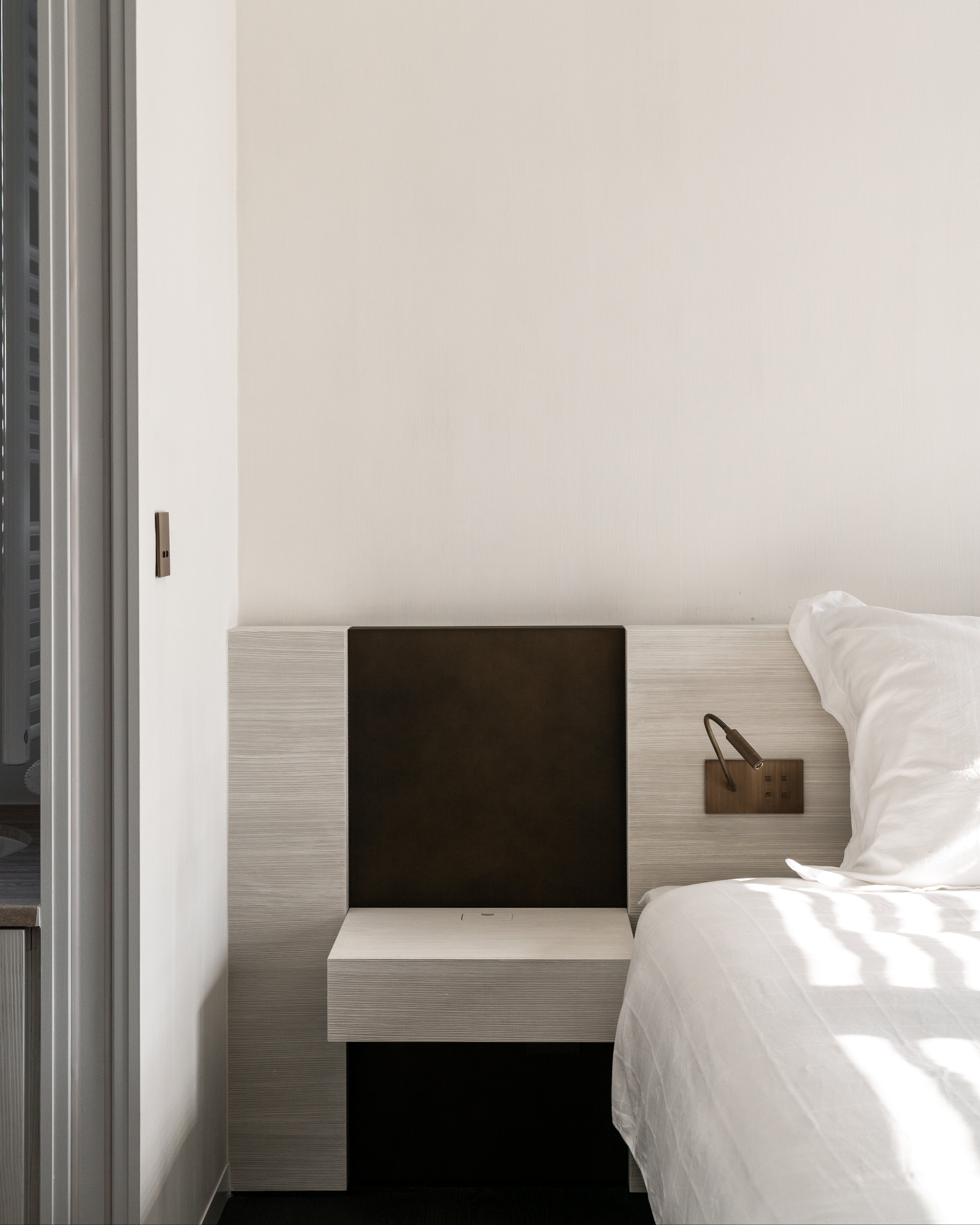 Modern bedroom with a bed and nightstand against a white wall.