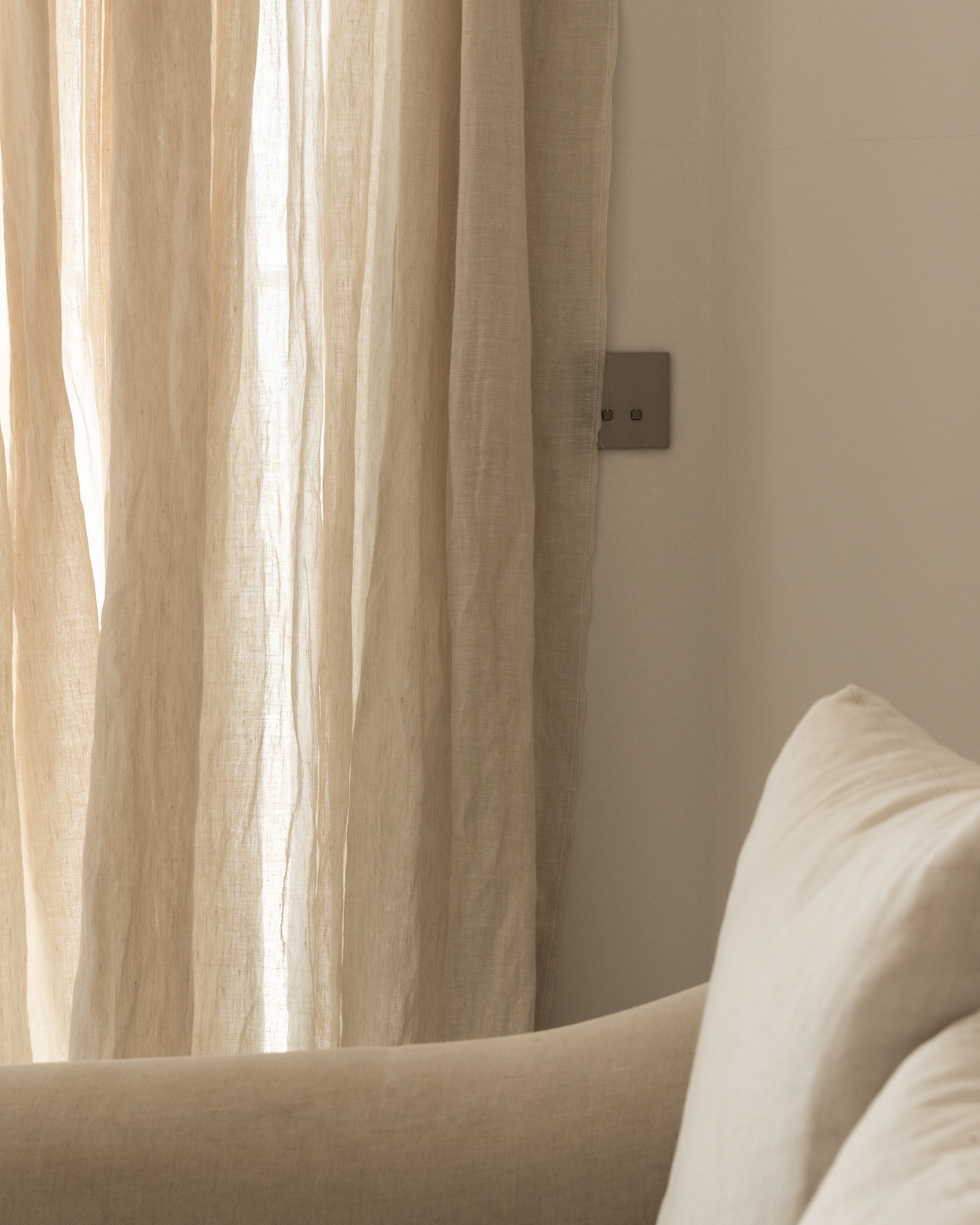 Beige sofa with cushions against a neutral wall with a curtain.