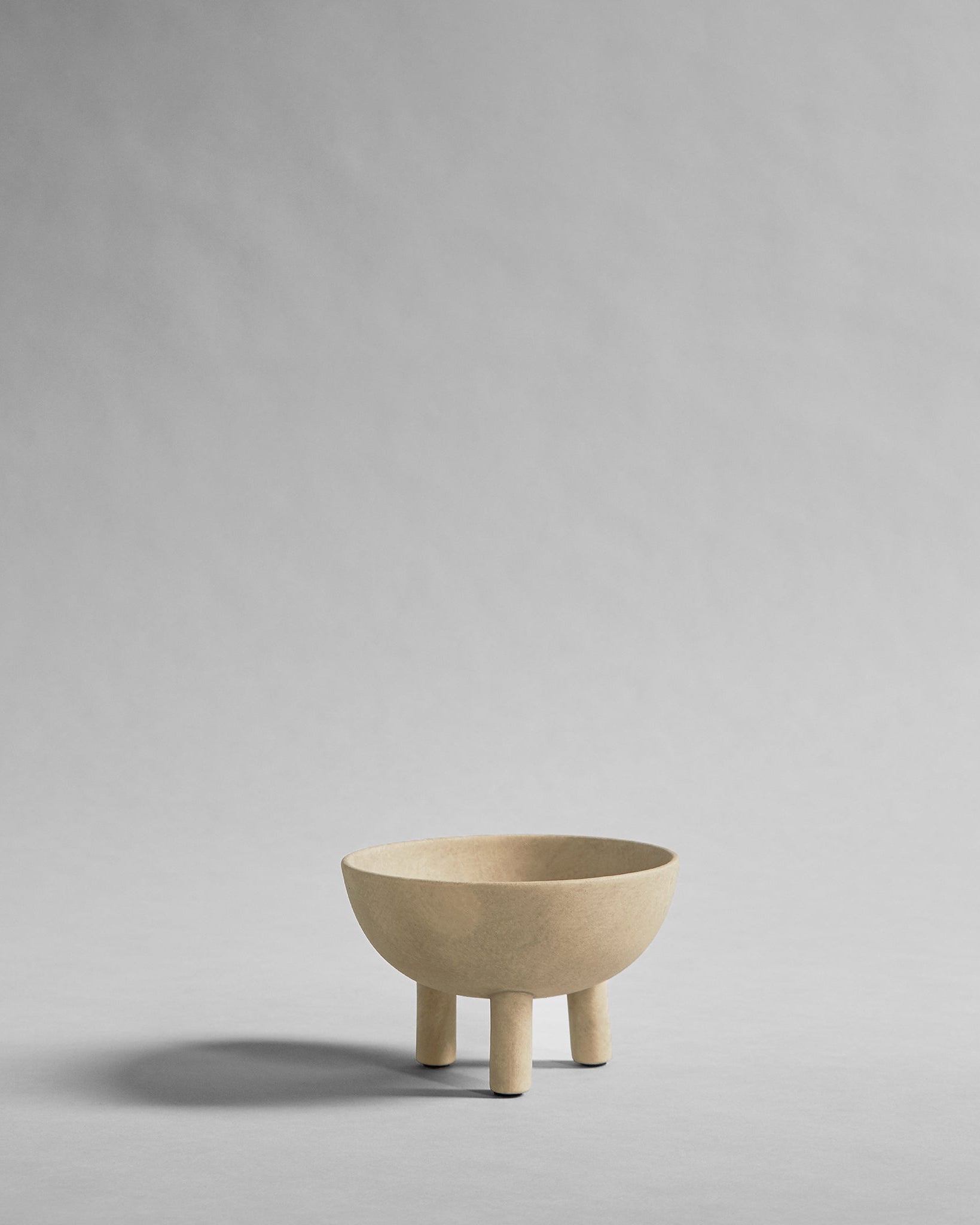 Beige ceramic bowl with three legs on a gray background