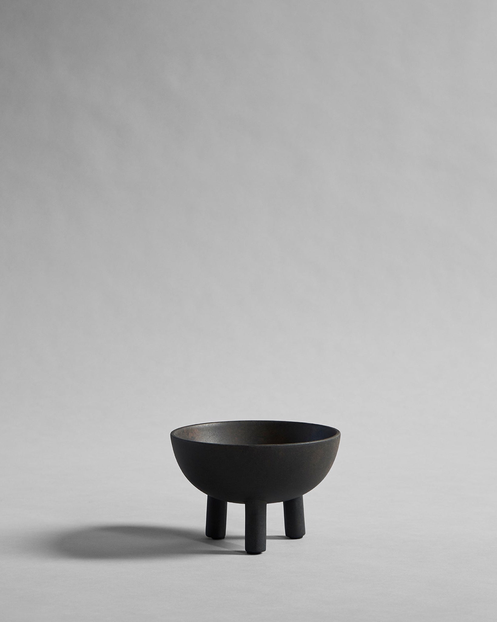 Black ceramic bowl on coffee color by 101 Copenhagen on a gray background