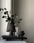 Decorative setup with black vase, books, and bowls on a shelf against a neutral wall.