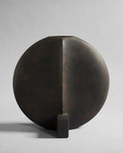 Bronze coffee color sculpture vase of a half-circle with a rectangular base on a gray background. Guggenheim Vase by 101 CPH curated by Numa Home