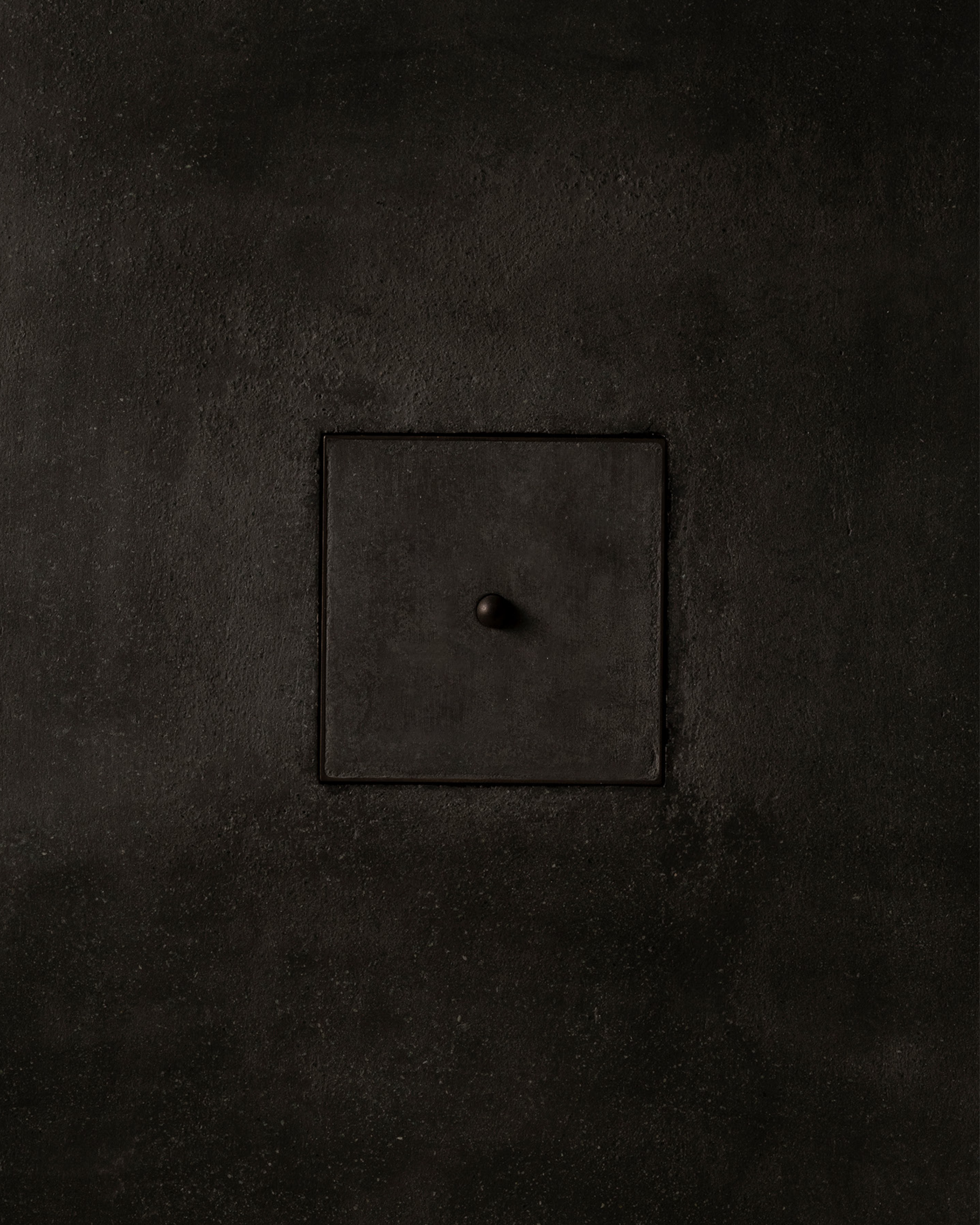 MATA recessed switch with a single bullet-shaped button, seamlessly integrated into a dark textured plaster wall – Sumum x Studio STRAF. Curated by Numa Home for the Netherlands and Turkey
