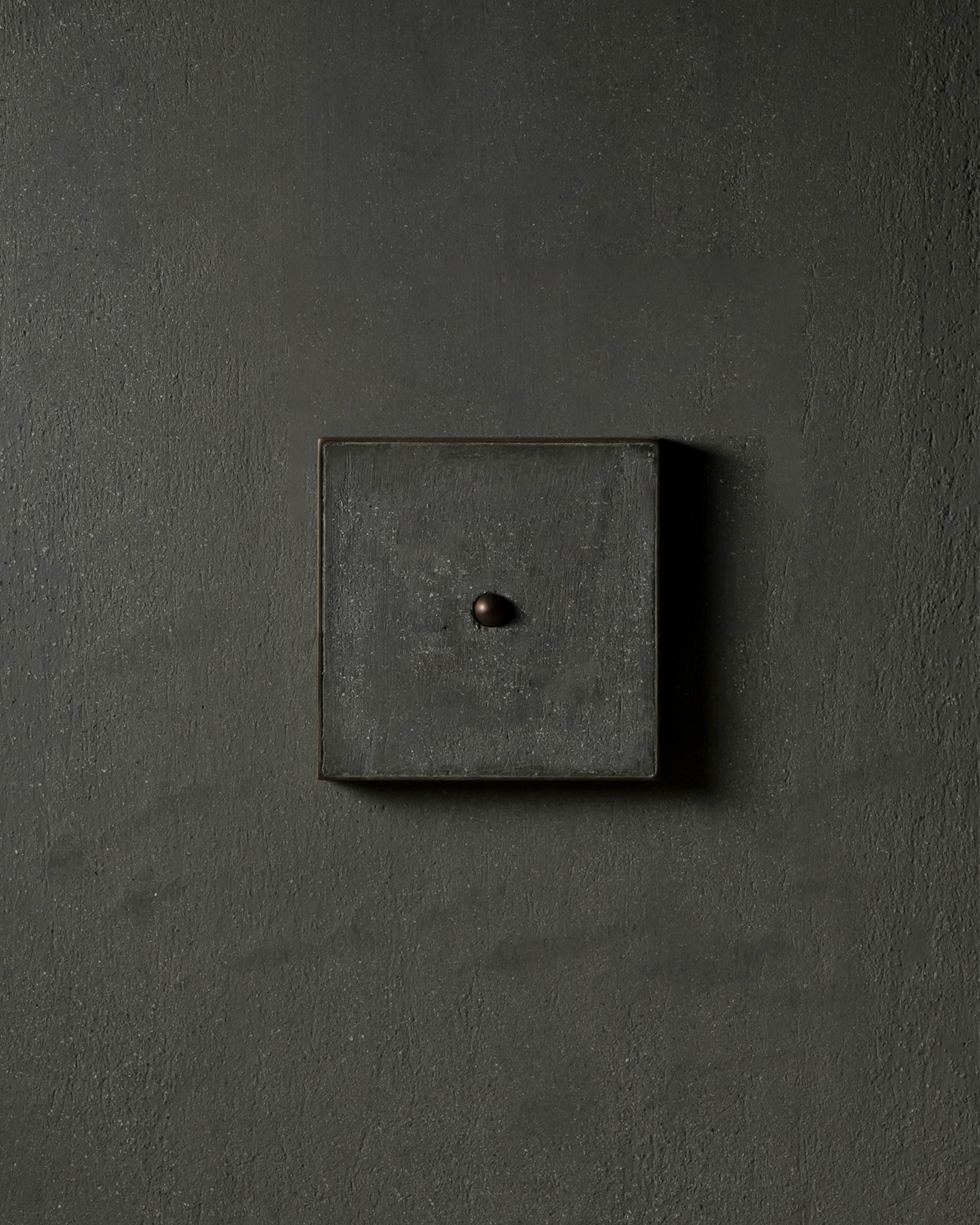 Surface-mounted MATA switch with a single bullet-shaped button on a dark textured wall plaster – Sumum x Studio STRAF. Curated by Numa Home for the Netherlands and Türkiye Markets.