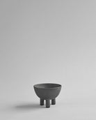 Dark gray ceramic bowl with three legs on a light gray background