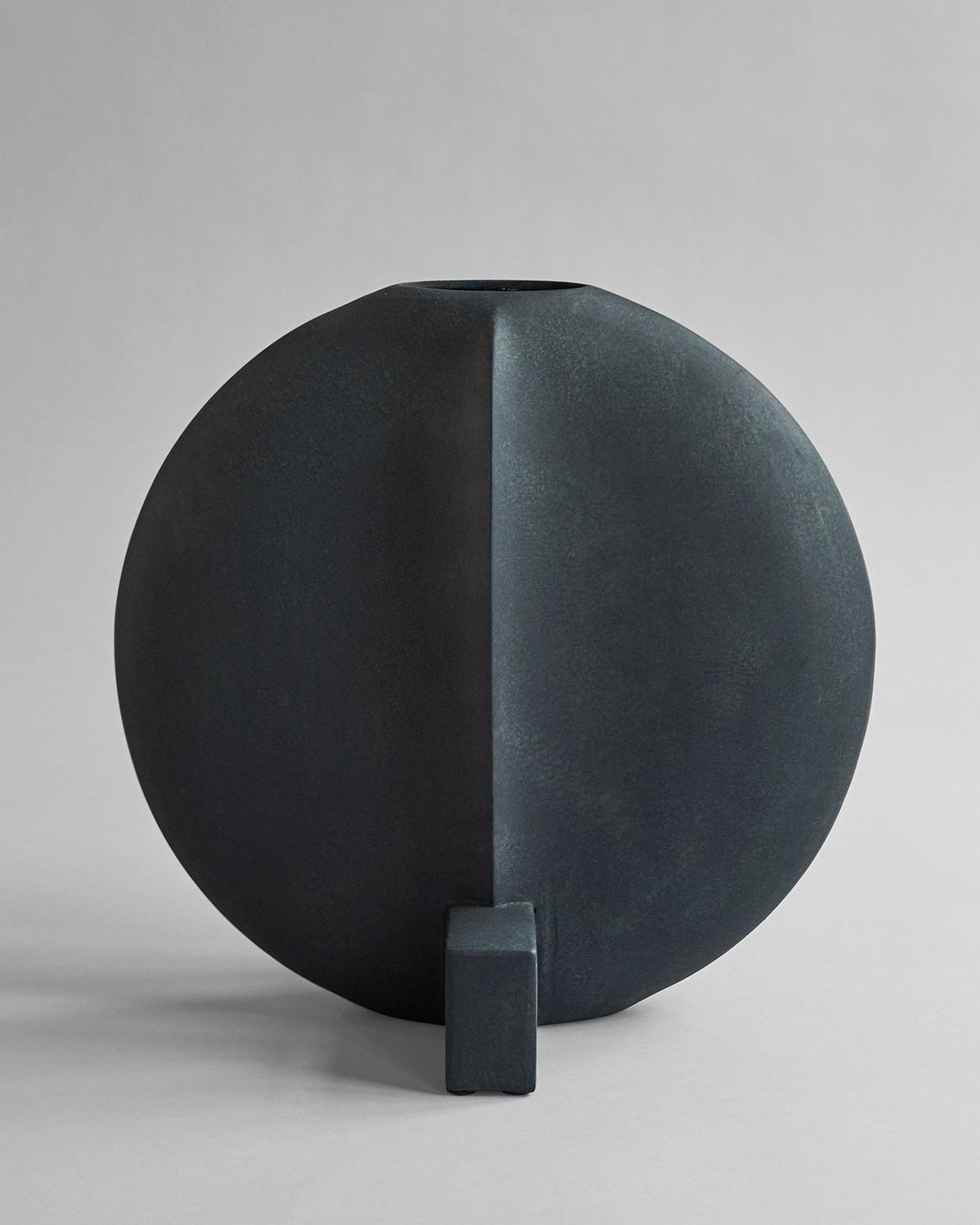 Black spherical scuptural vase with a rectangular base on a gray background.  Guggenheim Vase by 101 CPH curated by Numa Home