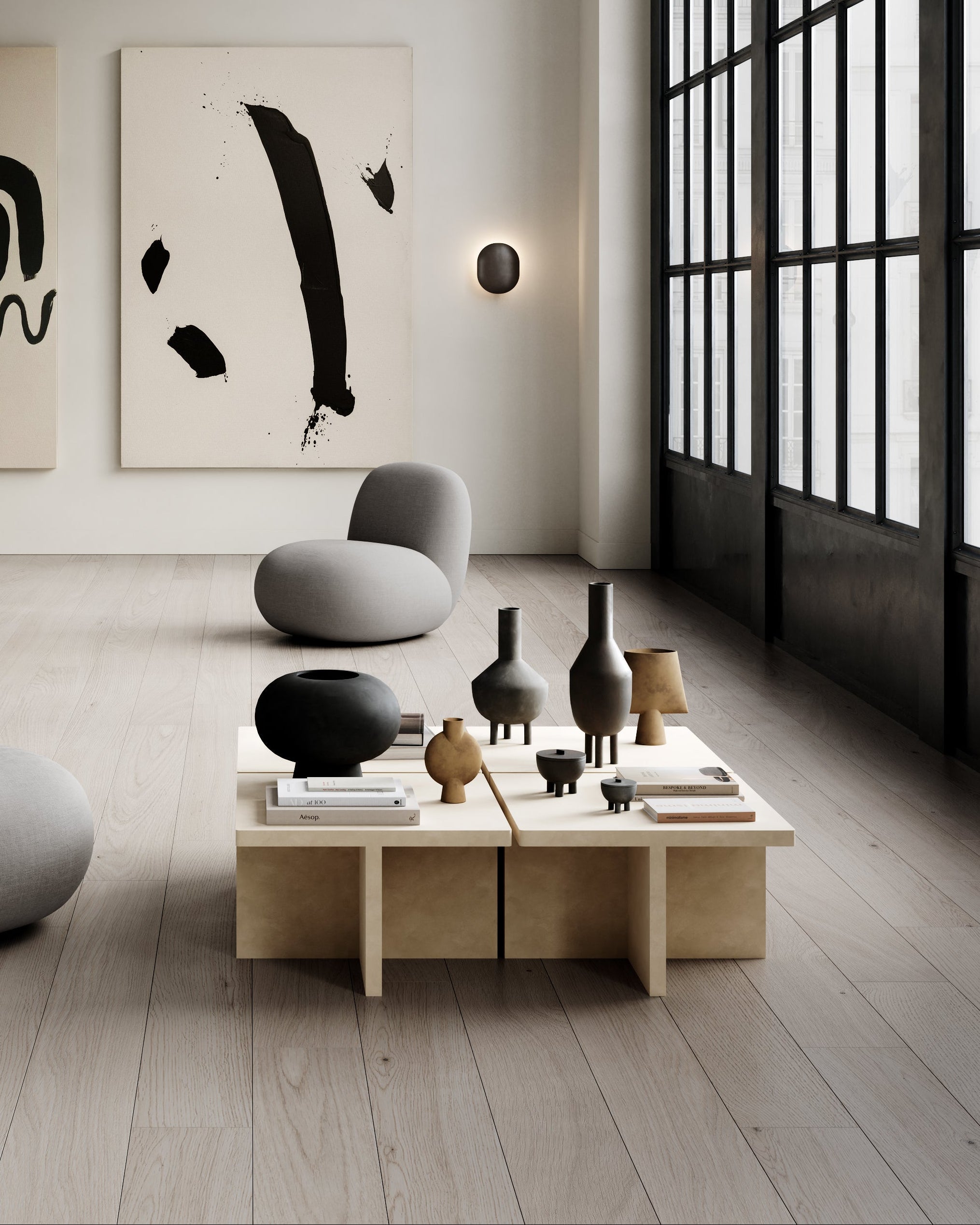 Modern living room with minimalistic decor, large windows, and abstract art on the wall. Four sand-colored 101 Copenhagen Brutus coffee tables are in front of the grey seat.