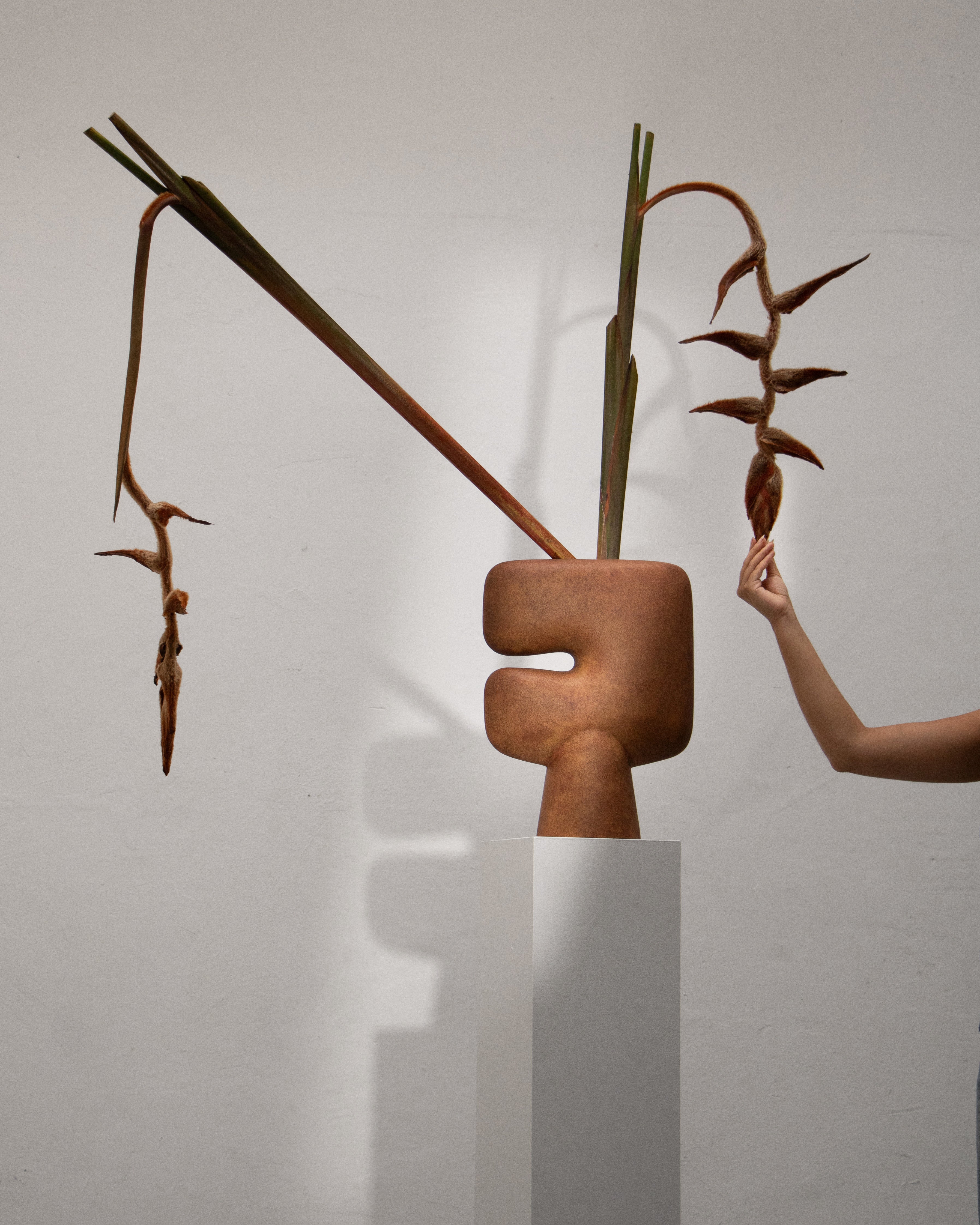 Ceramic sculpture with natural elements on a white pedestal against a plain background