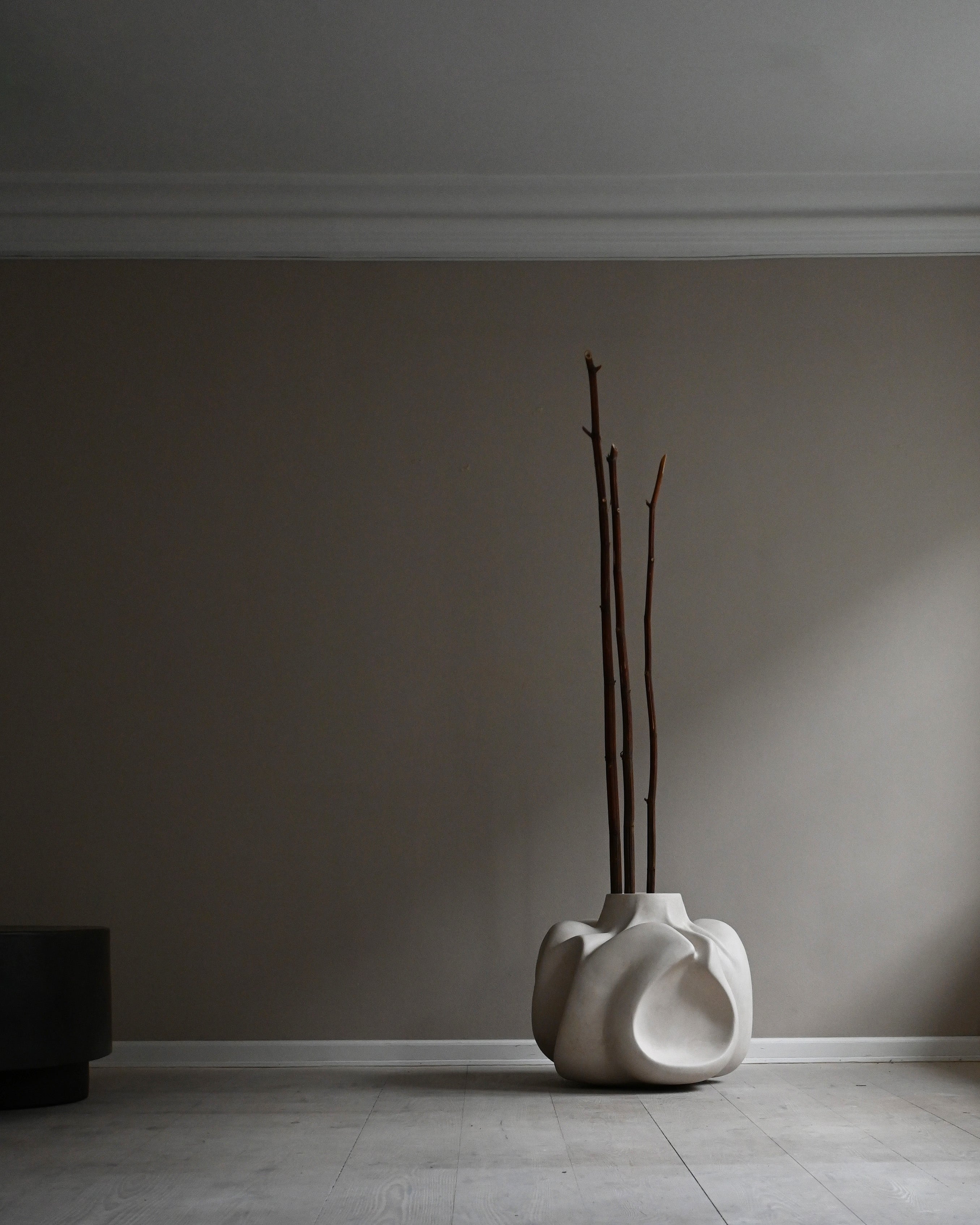 White sculptural vase with branches against a gray wall