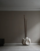 White sculptural vase with branches against a gray wall