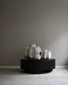 Three white ceramic sculptures on a black pedestal against a gray wall.