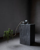 Decorative plant and stone sculpture on a dark pedestal against a dark background