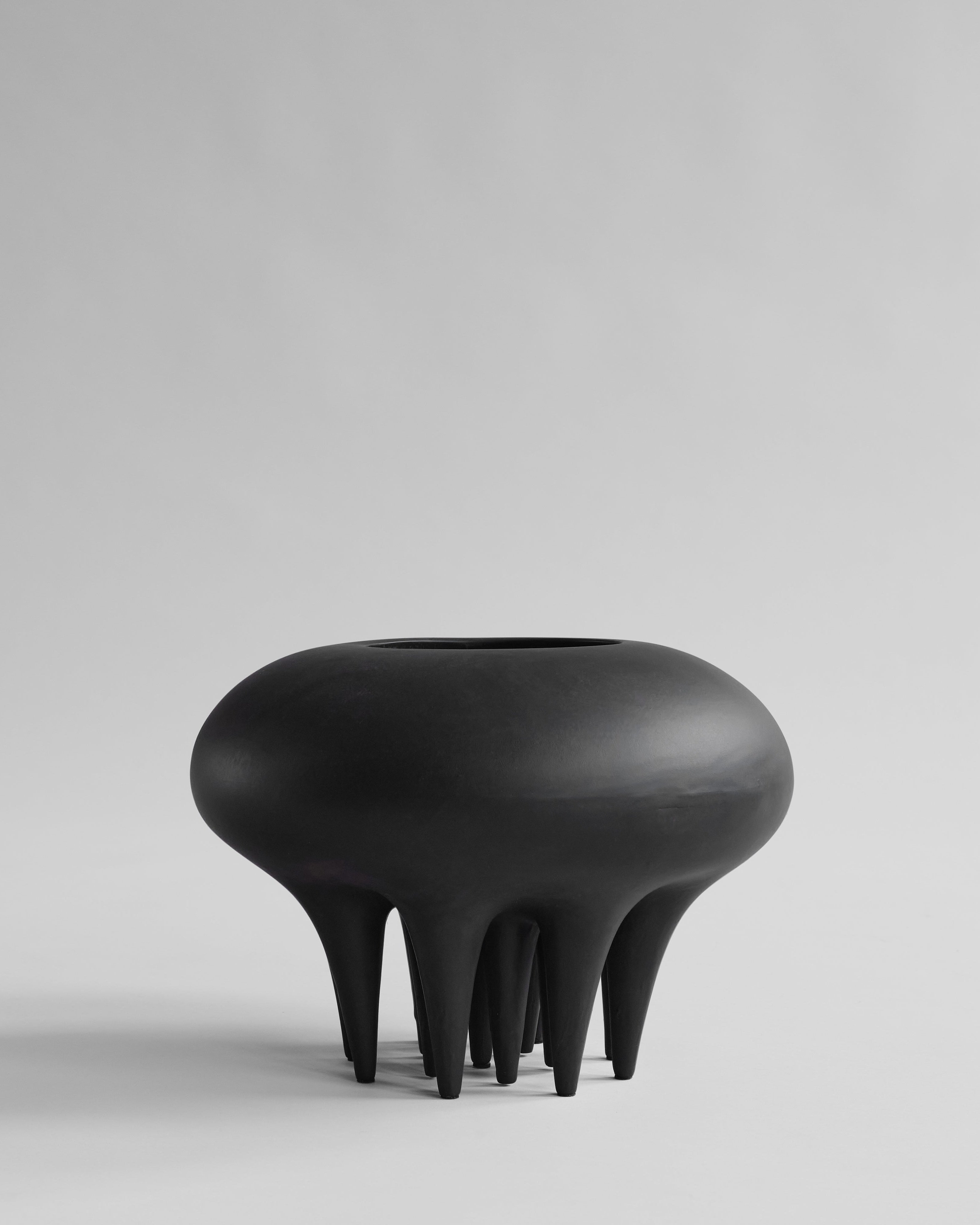 Black, abstract-shaped vase on a light gray background. Medusa Vase, Big by 101 Copenhagen. Sculptural ceramic vase with soft oval shapes and small conical legs, hand-glazed in Coffee. Curated by Numa Home for calm, modern interiors.