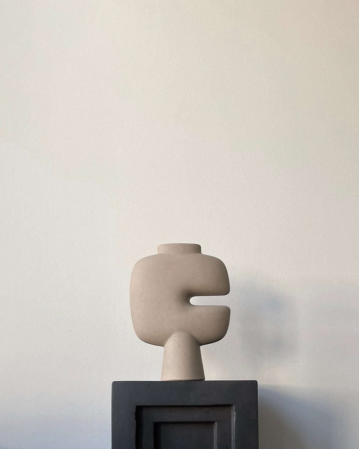 Abstract sculpture like vase, on a stand against a plain wall. Looks like an art piece.