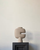 Abstract sculpture like vase, on a stand against a plain wall. Looks like an art piece.