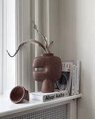 Decorative sculptural brown vase with a unique design on a shelf with books and a radiator.