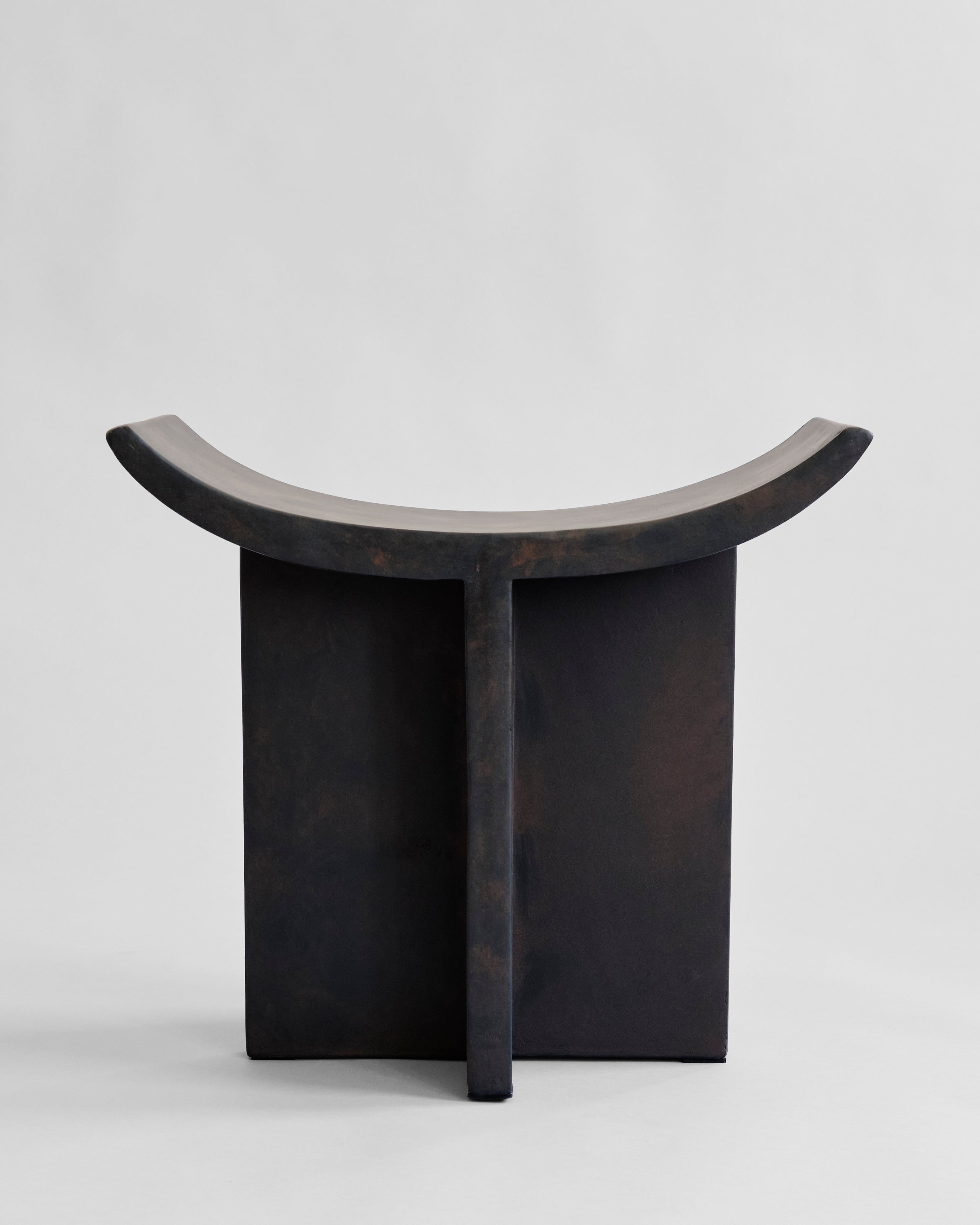 Black stone like stool with curved top on a light gray background