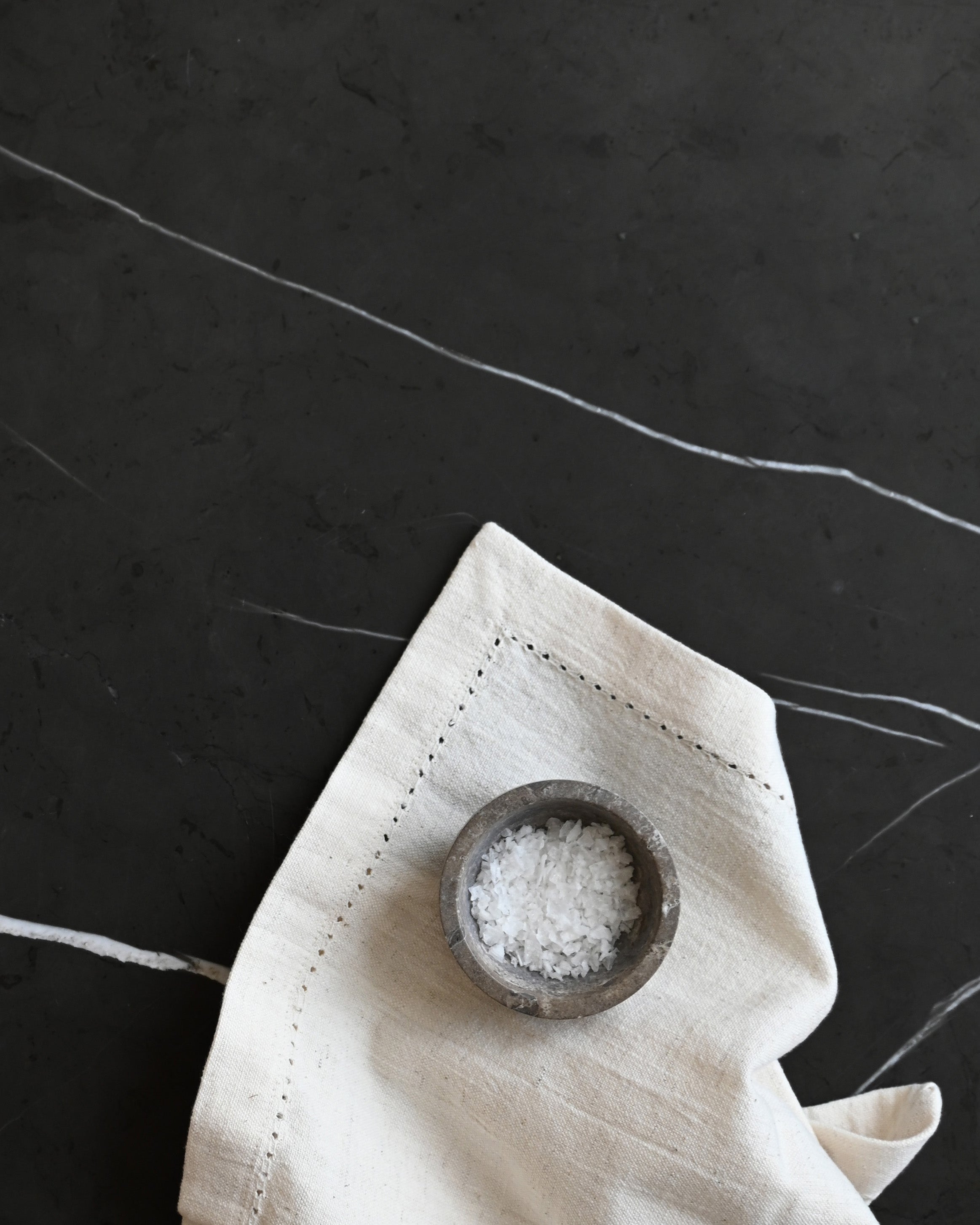 Small wooden bowl with salt on a white napkin against a dark background