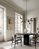Modern dining room with a black table and chairs, white walls, and large windows. Katachi Vase, Medio by 101 Copenhagen. Sculptural vase inspired by Japanese “shape”, available in High Glaze Birch ceramic and Clear or Smoked Forest mouth-blown glass. Fully waterproof – curated by Numa Home.
