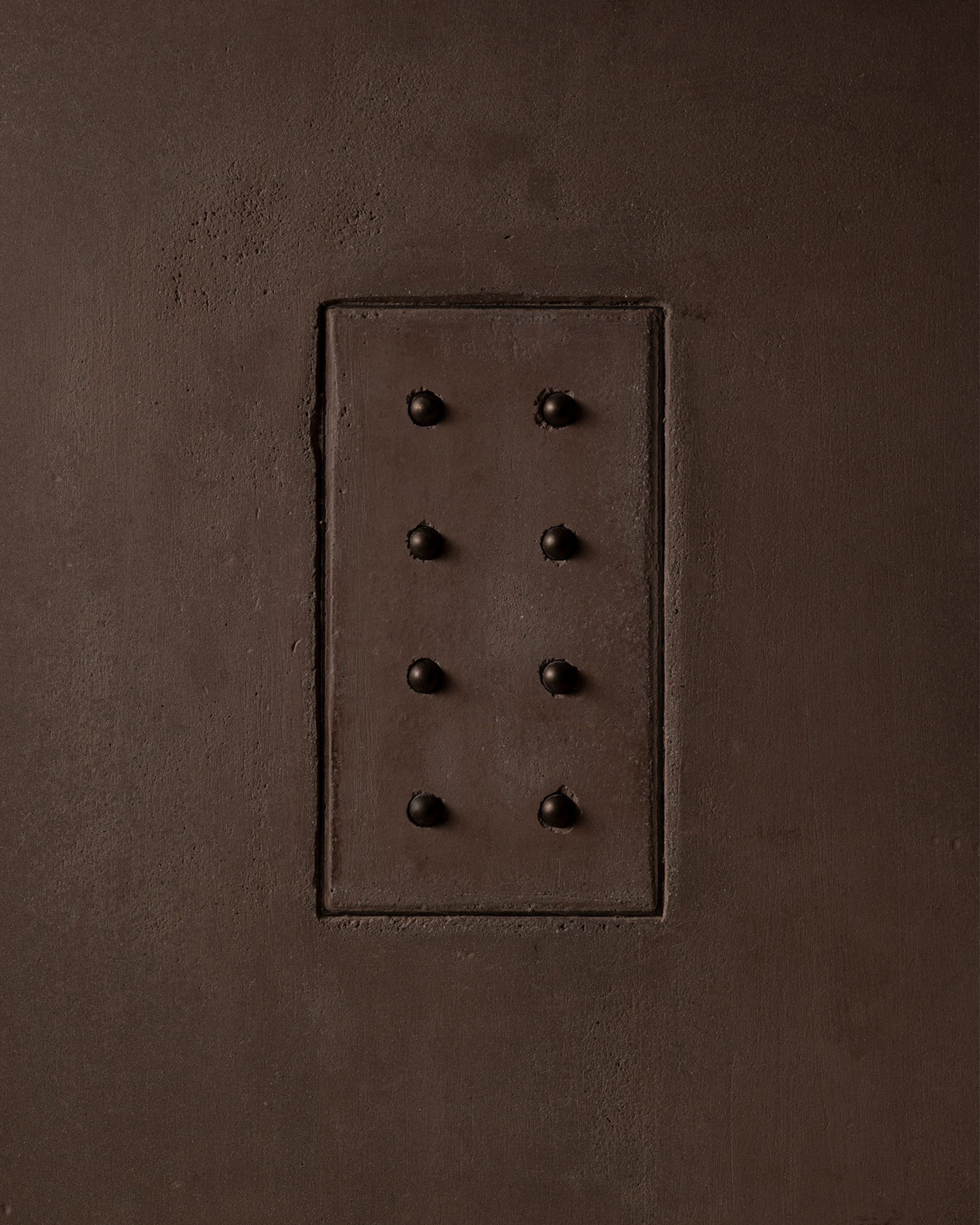 MATA recessed switch with eight bullet-shaped button, seamlessly integrated into a dark clay cloured and rough textured plaster wall – Sumum x Studio STRAF. Curated by Numa Home for the Netherlands and Turkey