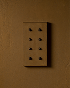 Surface-mounted MATA switch with eight bullet-shaped button on a mustard color micro cement textured wall plaster – Sumum x Studio STRAF. Curated by Numa Home for the Netherlands and Türkiye Markets.