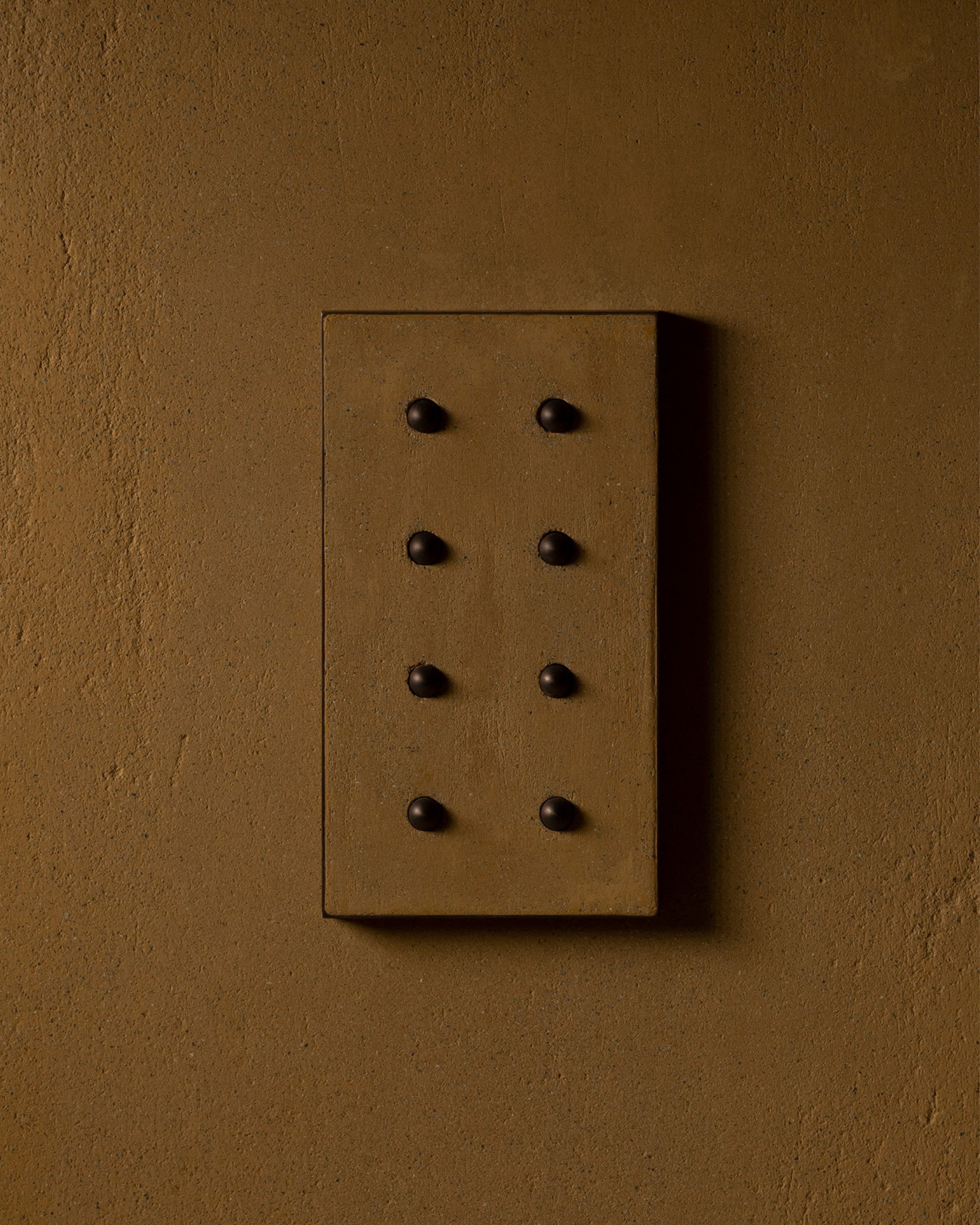 Surface-mounted MATA switch with eight bullet-shaped button on a mustard color micro cement textured wall plaster – Sumum x Studio STRAF. Curated by Numa Home for the Netherlands and Türkiye Markets.