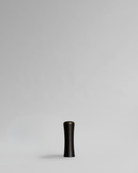 Black cylindrical brass cabinet handle on a light gray background. Brass cabinet handle designed by Stef Claes, created by Sumum, curated by Numa Home.