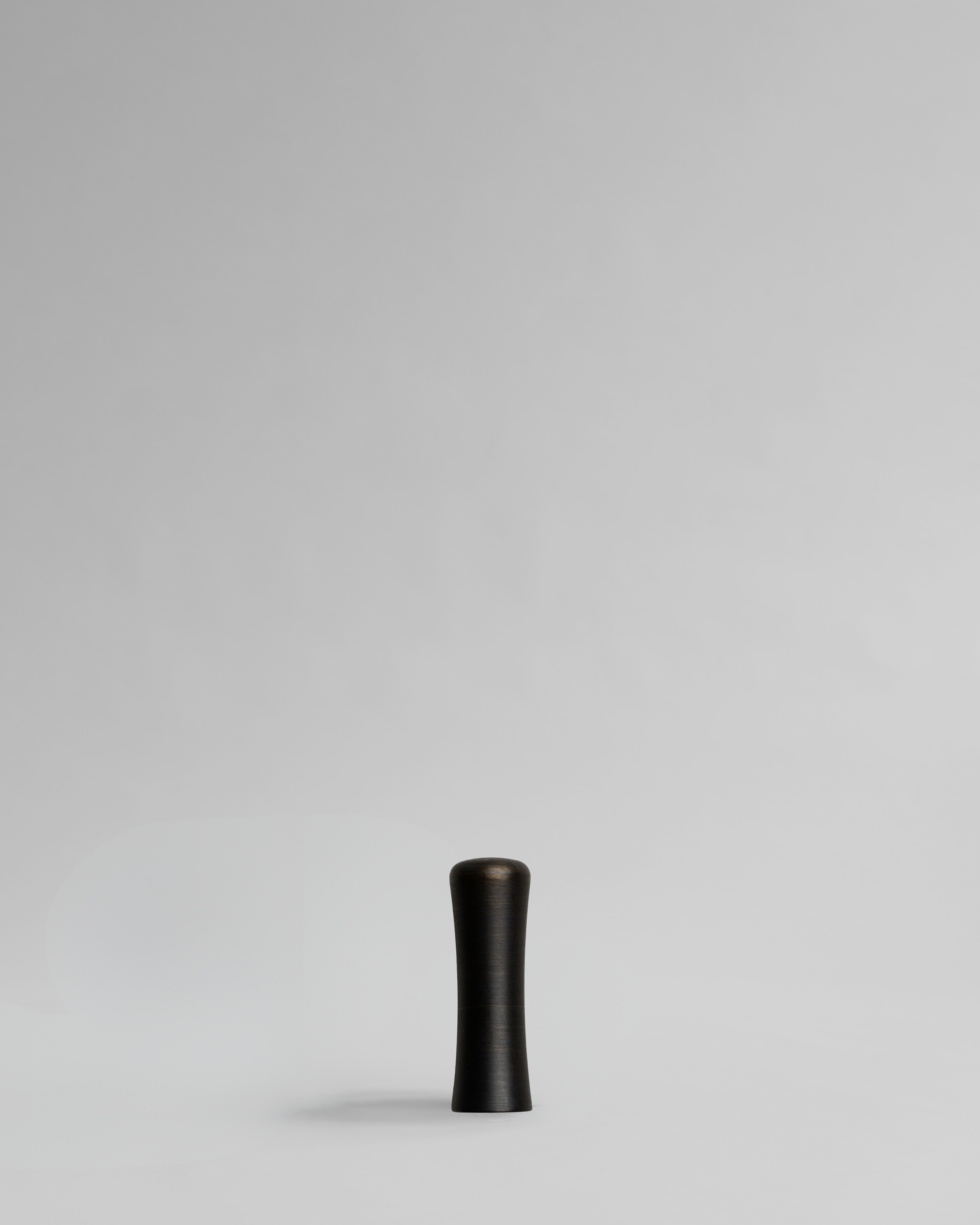 Black cylindrical brass cabinet handle on a light gray background. Brass cabinet handle designed by Stef Claes, created by Sumum, curated by Numa Home.