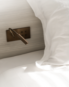 Close-up of a bed with white bedding and a brass reading light in brushed brass patina with 4 push buttons.