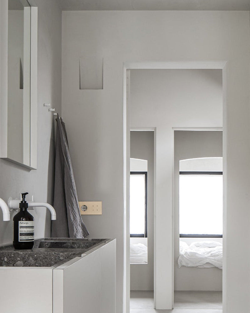 Bathroom interior with sink, mirror, and towel, leading to a bedroom. Brushed brass sumum outlet with 4 PIN push buttons. Curated by Numa Home
