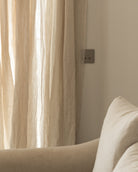 Beige sofa with cushions against a neutral wall with a curtain.