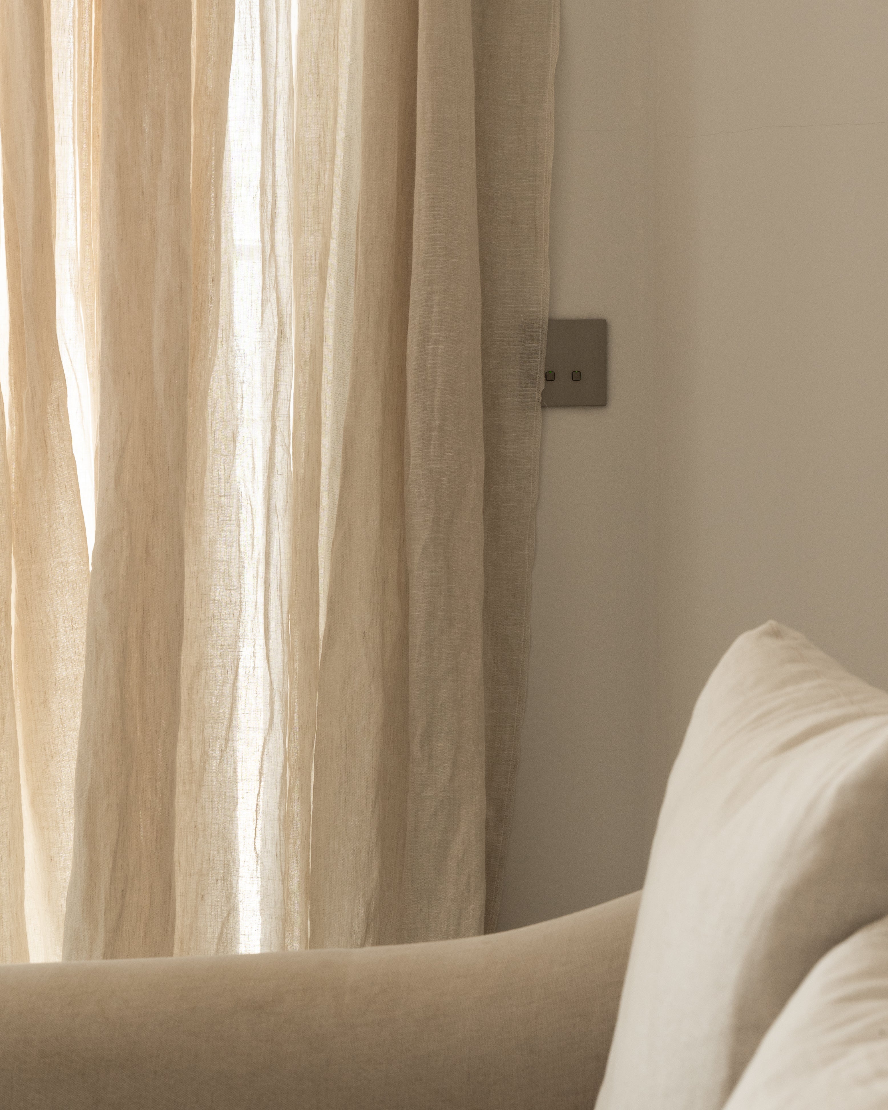 Beige sofa with cushions against a neutral wall with a curtain.