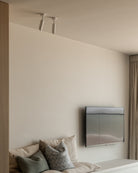 Modern living room with a television mounted on the wall, a sofa with pillows, and a window with curtains. White brass ceiling light fixture with bevelled nose. Sumum brass spotlights made from brass partnered with PSM Lighting