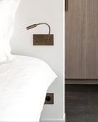 Bedroom with wooden wardrobe and white bedding. Brass reading light in brushed bronze patina with 4 buttons to control the lights.