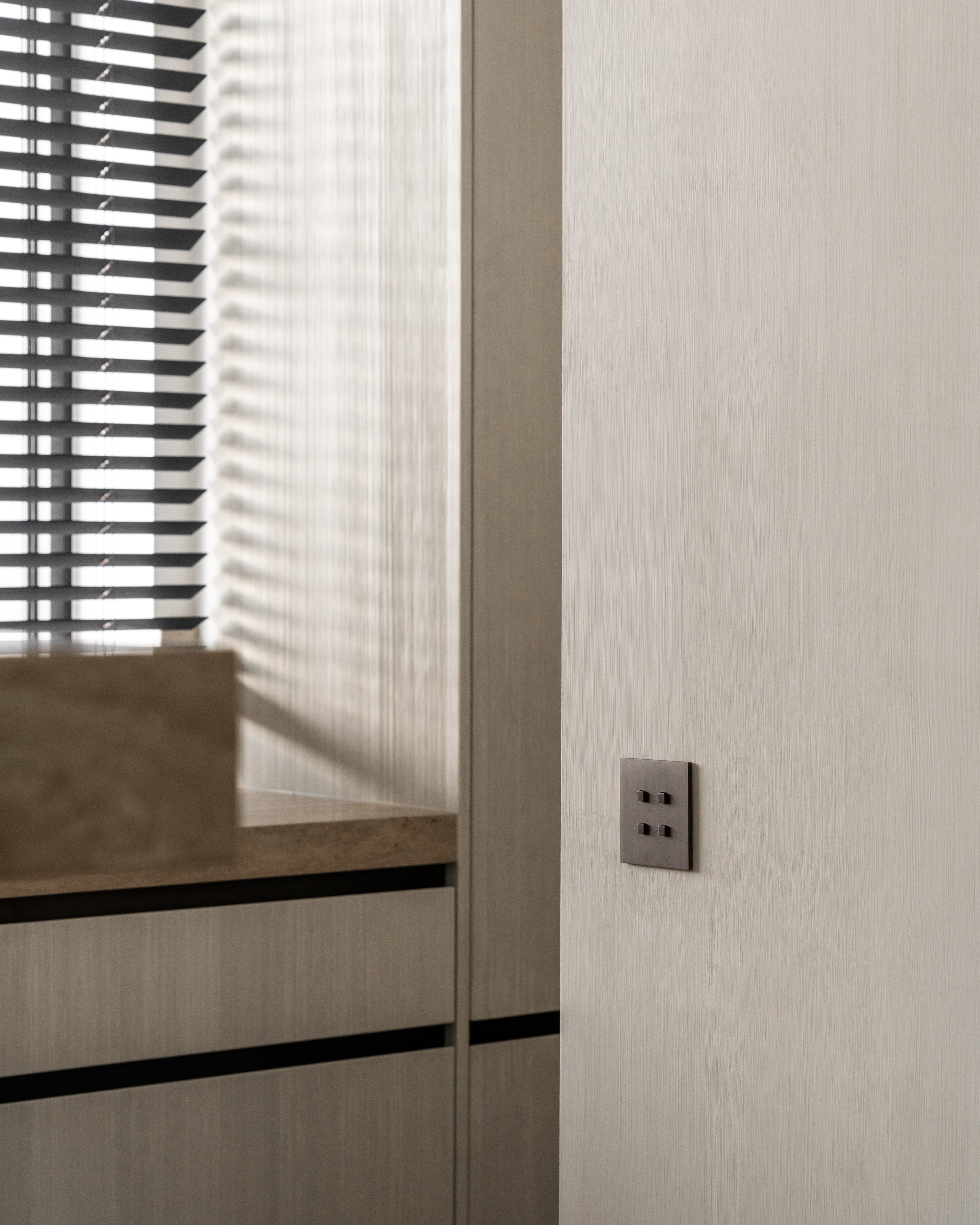 Sumum Square handcrafted brass switch in dark brushed finish, installed on a modern Dutch kitchen wall, premium custom light switch provided by Numa Home